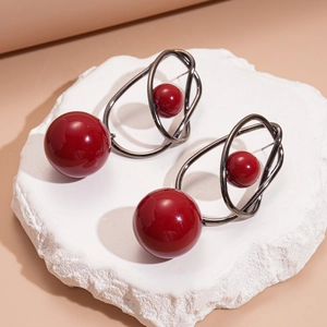 Detailed shot of geometric acrylic earrings with red beads on a textured white stone