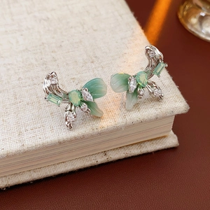 Macro shot of silver bow earrings with light green stones and zircon on a textured book