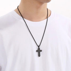 Détail d'un pendentif double croix noire avec chaîne torsadée porté sur un t-shirt blanc