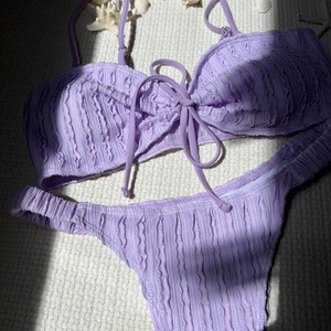Detailansicht eines lila Seersucker-Bikinis mit Schleifendetail und Meeresmuscheln