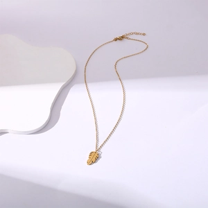 Elegant gold leaf pendant necklace in stainless steel on minimalist display base
