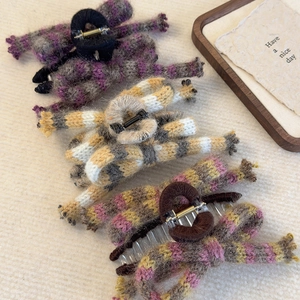 Detailed view of three knitted bow hair claws with colorful stripes on a beige fabric background