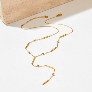 Detailed view of a gold Y-shaped necklace with bar pendant and metal beads on a stone
