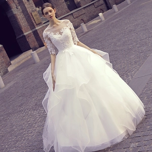 Elegant white lace wedding dress with long sleeves and layered tulle skirt in outdoor setting