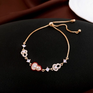 Detail of adjustable gold-tone bracelet with red heart enamel and white zircon inlay