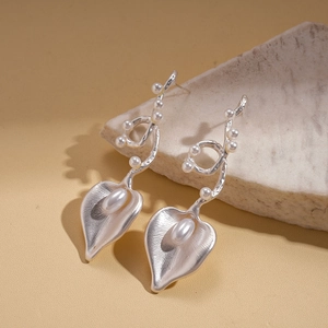 Macro shot of silver metal calla lily earrings with white pearls on stone texture