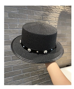 Close-up of black straw boater hat featuring pearl accents and metal rivets on the band