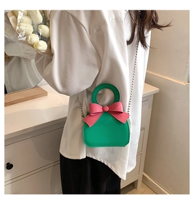 Mini green and pink crossbody bag with bow detail and gold chain on model's back
