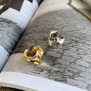 Close-up of irregular liquid metal ear cuffs in gold and silver on a minimalist magazine