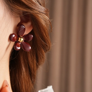 Detail view of a model wearing a burgundy floral earring with a golden center