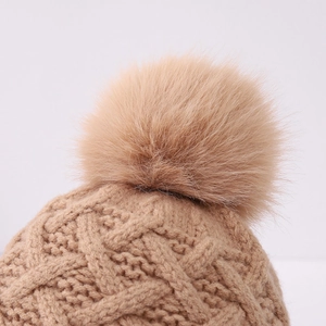 Detail view of khaki knit winter hat with fluffy pom-pom and diamond cable stitch texture