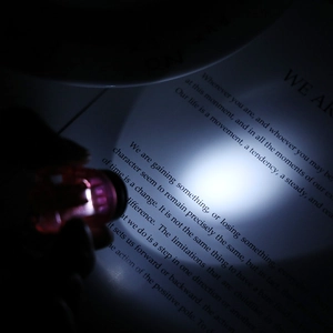 Detail of pink mini LED flashlight keychain illuminating book text with cold white light