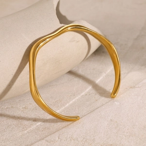 Detailed view of gold plated wavy cuff bracelet resting on textured ceramic stone
