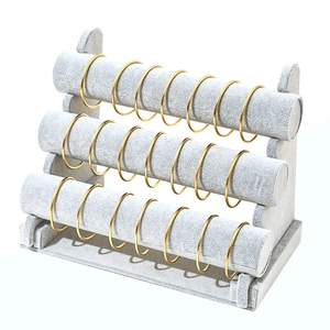 Three-tier grey velvet jewelry stand displaying gold bracelets on a white background