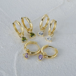 Macro shot of three heart-shaped gemstone hoop earrings in gold with colorful crystals