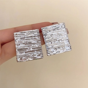 Silver square geometric earrings with textured metallic pleats held by hand