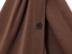 Macro detail of dark brown textured fabric and a black matte four-hole button on the vest