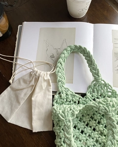Detail of mint green woven handbag with beige drawstring inner pouch on a wooden table