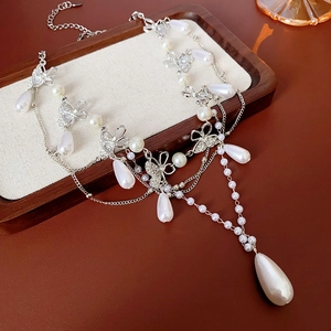Macro detail of layered silver necklace with butterfly charms and water drop pearls