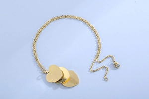 Détail d'un collier doré multicouche avec trois pendentifs cœurs et un fermoir mousqueton