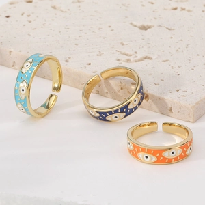 Three gold-plated evil eye enamel rings in light blue, dark blue and orange on stone