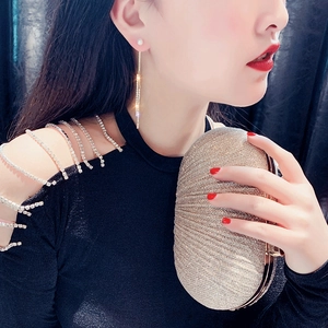 Champagne gold evening clutch bag with radial pleats and pearl tassel earrings on a model