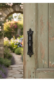 Detail showing vintage black cast iron door handle with fleur-de-lis design on wood