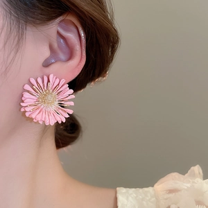 Close-up of pink raffia daisy stud earring worn by model for a beach vacation look