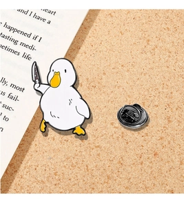 Macro detail of cartoon white duck enamel pin holding a knife on cork board background