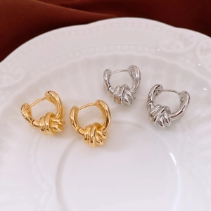 Macro detail of twisted knot earrings in gold and silver finish on a decorative plate