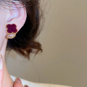 Close-up of a burgundy velvet clover stud earring with gold beaded trim on woman's ear