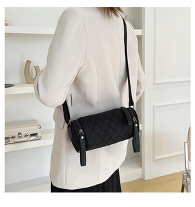 Minimalist black quilted cylinder crossbody bag styled with a cream blazer and long strap