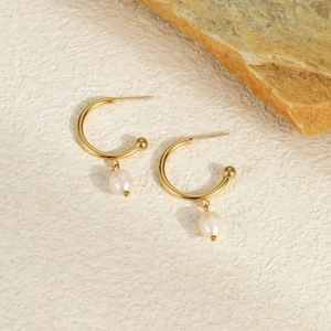 Detailed view of C-shaped gold hoop earrings with white pearls on a natural stone background