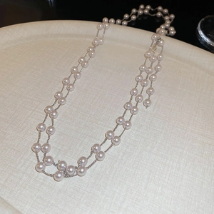Gros plan de colliers de perles superposés sur un plateau beige avec détails en métal