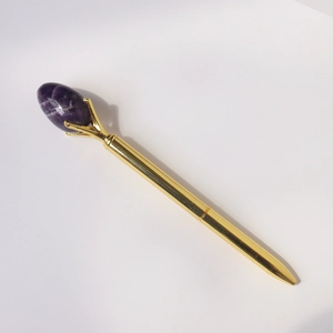 Detail of elegant gold metal ballpoint pen featuring a purple crystal gemstone top