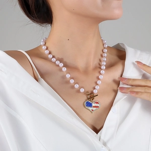 Detailed close-up of pearl necklace featuring USA flag heart pendant and gold toggle clasp