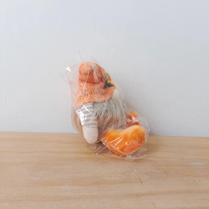 Detail of harvest gnome plush with orange knit hat in packaging on wooden surface