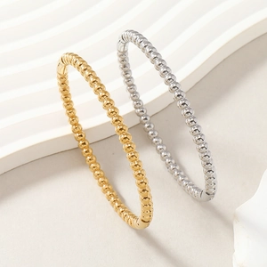 Dettaglio di braccialetti a sfere in oro e argento su sfondo beige strutturato