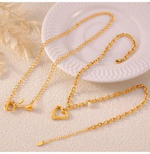 Gros plan d'un collier doré avec cœur ajouré, rose et perle blanche sur porcelaine