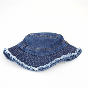 Detail of frayed edge denim bucket hat with dark blue fabric and metal badge