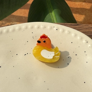 Mini acetate rooster hair clip with marble texture in a ceramic dish with plants