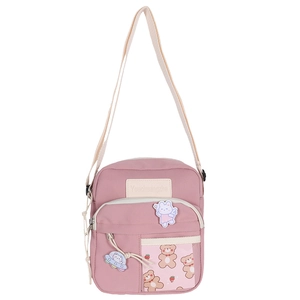 Détail du sac bandoulière rose avec écussons de dessins animés et pendentif ours