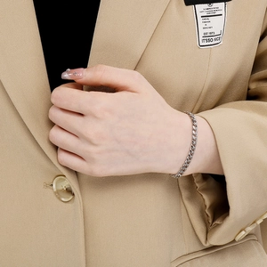 Polished silver Cuban link bracelet styled on wrist with beige blazer for a trendy look