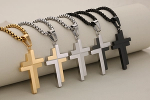 Five assorted cross pendants in gold, silver, and black finishes on a beige roll display