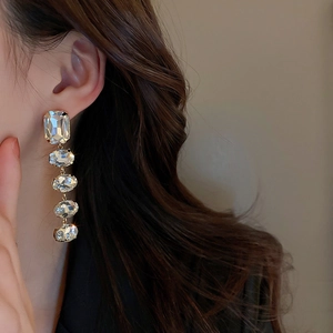 Macro detail of long silver needle earrings with clear crystals and gold plating
