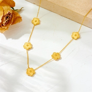 Detail of a gold clover charm necklace on a white textured background with roses