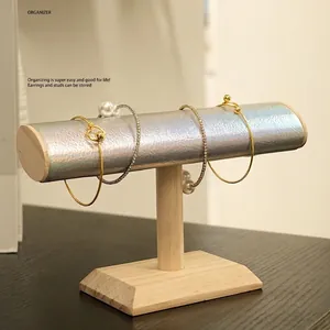 Minimalist T-bar jewelry display stand with light wood base and silver leather cylinder