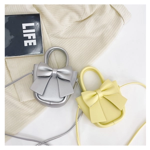 Close-up of silver and pale yellow bow crossbody bags with slender shoulder straps