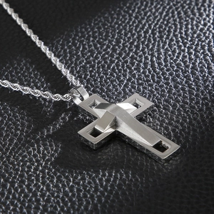 Close-up of a silver hollow double-layer cross pendant on a textured black background