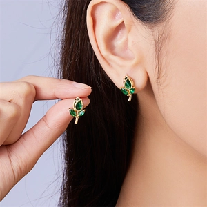 Close-up of gold flower stud earrings with green gemstones worn by a model